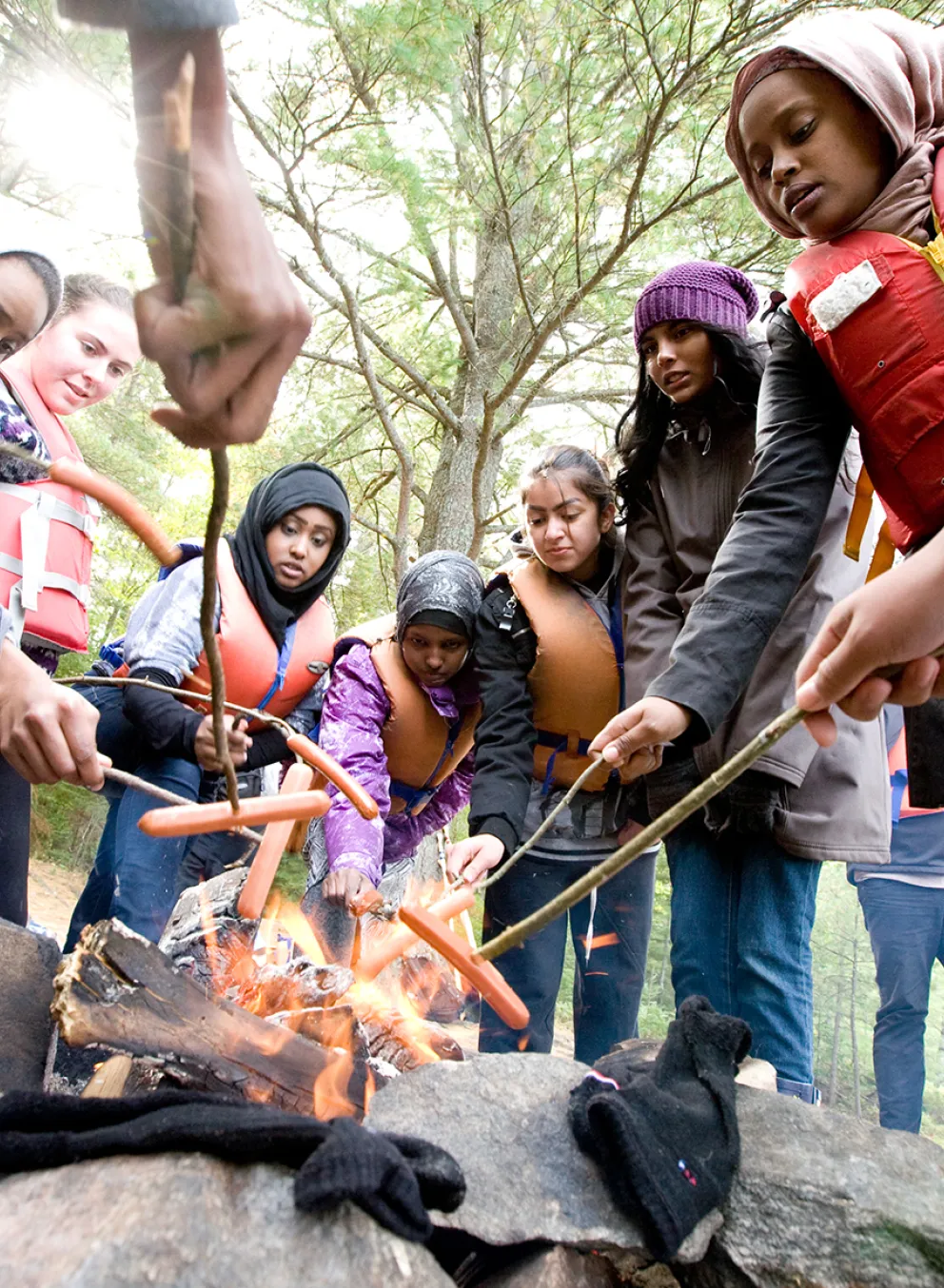 Youth roasting hotdogs on an open camp fire