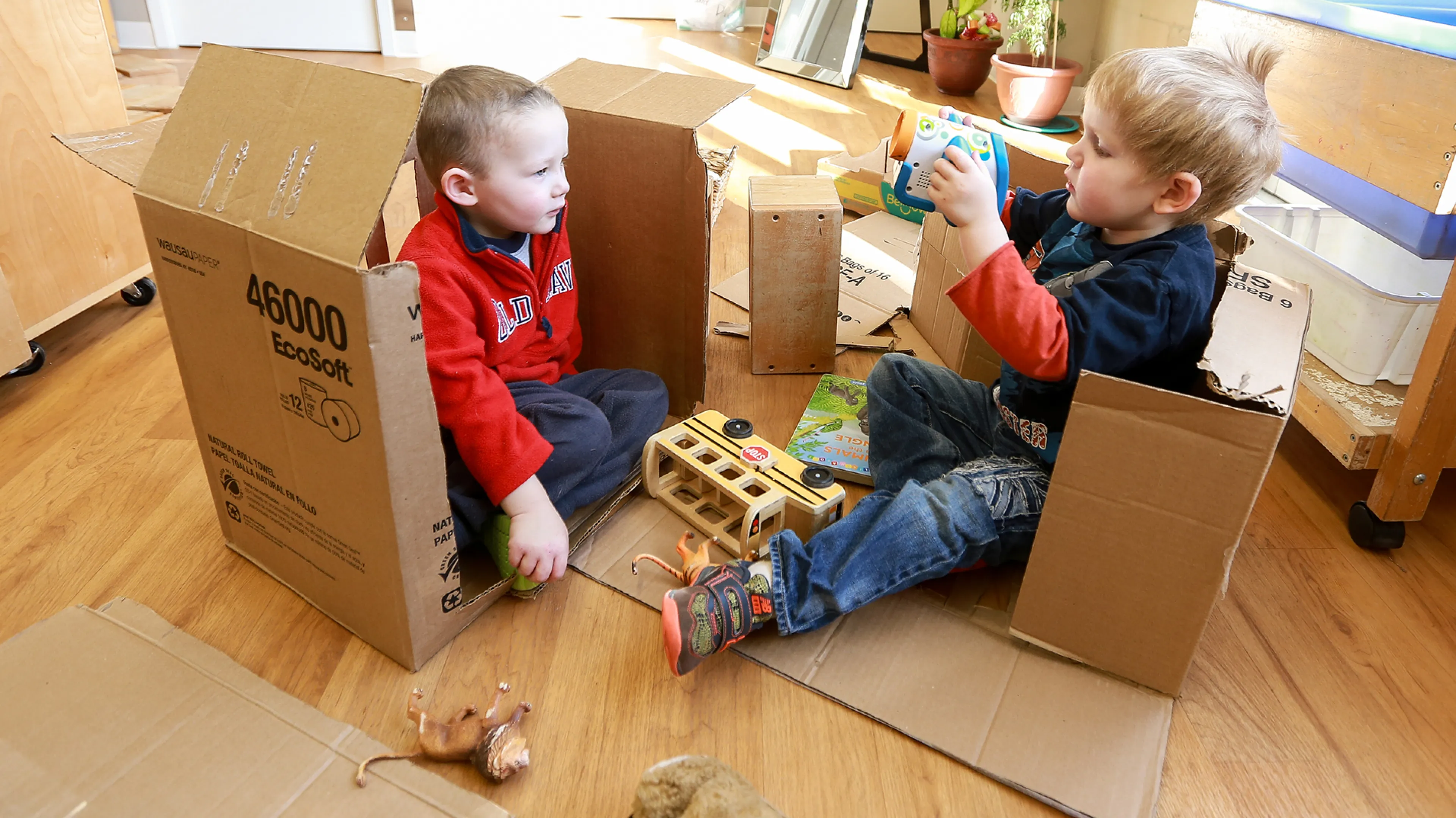 Two male preschool children building and playing with cardboard boxes